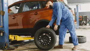 A mobile mechanic in blue overalls repairs a car in a garage setting.