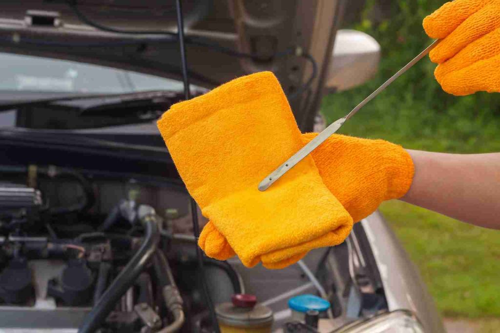 Mechanic wearing orange gloves checking car transmission fluid dipstick with cloth during maintenance