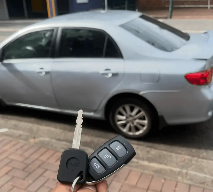 Hand holding a car key and remote fob in front of a parked silver sedan, showing a common situation when the remote won’t unlock the car.