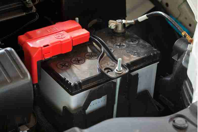 Close-up of a car battery with a red safety cover over the positive terminal.